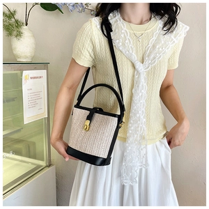 Detail of woven straw bucket bag with black leather trim and elegant gold metal clasp