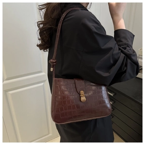 Detail of dark brown croc-embossed underarm bag with gold lock and knotted strap