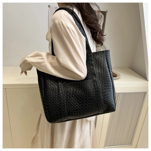 Detail of a black woven leather tote bag shown on model in a minimalist setting