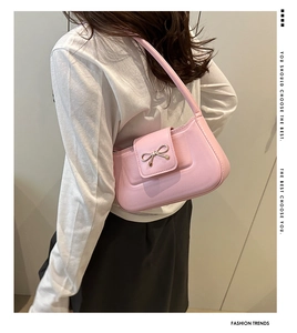 Detail of pink baguette bag with golden metal bow buckle on a model's shoulder