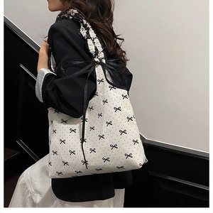 Detail of canvas tote bag featuring black bow patterns and elegant ruffled shoulder straps
