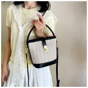 Detail of woven bucket bag featuring black leather trim and elegant gold metal twist lock