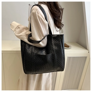 Close-up of a black woven tote bag showing the intricate texture and shoulder strap fit
