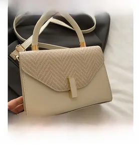 Detail of elegant beige handbag featuring woven straw flap and gold rectangular buckle