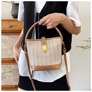 Detail of hand-woven straw bucket bag with brown leather trim and golden metal clasp