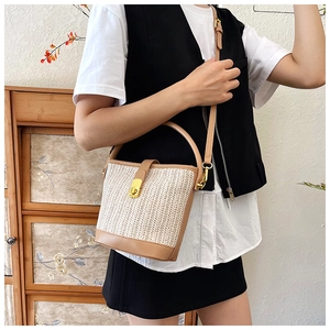 Detail view of woven straw bucket bag with brown leather trim and gold metal clasp