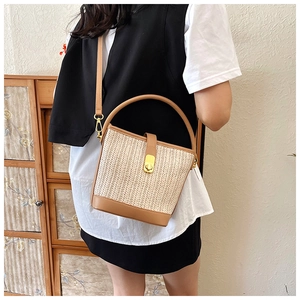Straw bucket bag with brown leather trim and gold twist lock shown in a lifestyle setting