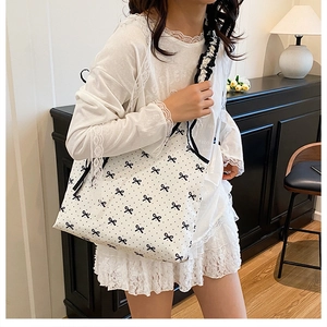 Detail of white canvas tote bag with black bow print worn over the shoulder by a model
