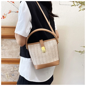 Close-up of woven straw bucket bag with brown leather trim and golden metal lock