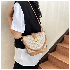 Detail of woven straw bucket bag featuring brown leather trim and golden metal lock