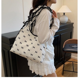 Detail of white canvas shoulder bag featuring black bow patterns and ruffled strap design