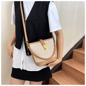 Detail of woven straw bucket bag showing leather trim and golden metal swivel lock