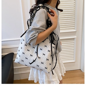 Close-up of white canvas tote with black bow prints and ruffled shoulder strap