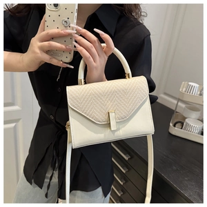 Detail of a chic cream handbag featuring a woven straw flap and gold metal lock hardware