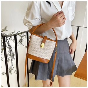 Detail of woven straw bucket bag with brown leather trim and golden twist lock