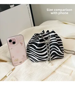 Detail view of zebra pattern bucket bag with chain strap and phone size comparison