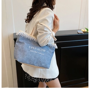 Detail of blue denim tote bag with white lace trim and printed lettering on white suit