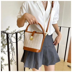 Detailed shot of the woven straw bucket bag with brown leather trim and golden twist lock