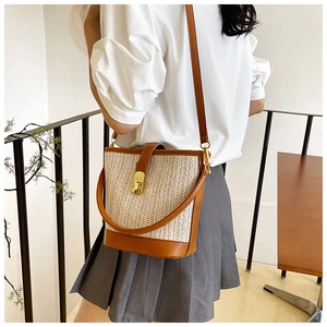Detail shot of the woven straw bucket bag with leather trim on model at side angle