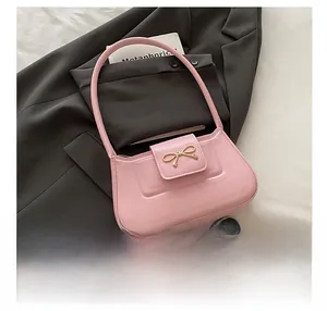Detailed close-up of a pink shoulder bag with a gold bow buckle on a stylish suit backdrop