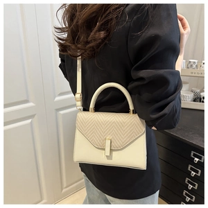 Detail of beige crossbody bag showing woven flap texture and gold hardware on model
