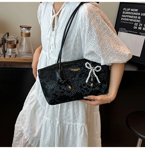 Detail of black snake-embossed shoulder bag with a pearl bow charm and gold logo