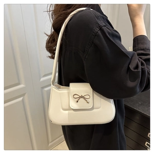 Close-up of white faux leather shoulder bag with a vintage golden bow metal clasp detail
