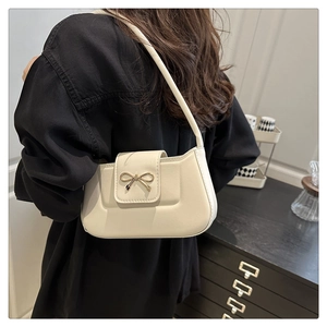 Detail of cream leather shoulder bag with gold bow clasp on elegant black outfit