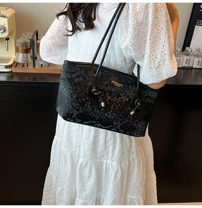 Detailed close-up of a black snakeskin textured tote bag with gold lettering and metal accents