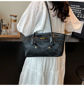 Detail of black tote bag with python texture and gold lettering on white lace dress