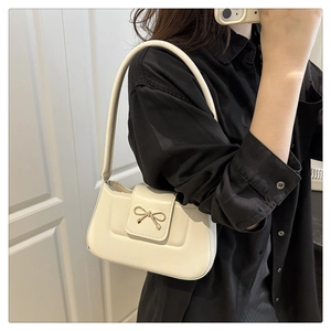 Détail d'un sac baguette crème avec un fermoir nœud en métal doré et une texture en PU