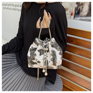 Close-up of cow print bucket bag featuring gold chain strap and elegant pearl charm detail