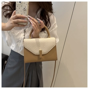 Detail of a brown leather crossbody bag with beige woven texture and gold metal lock