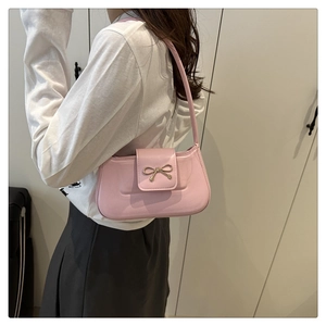 Detail of pink shoulder bag featuring a decorative golden metal bow on smooth leather