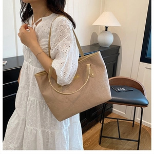 Détail d'un grand sac cabas beige gaufré porté par un mannequin dans un décor d'intérieur