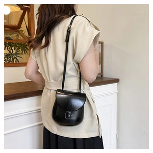 Close-up of black glossy leather saddle bag worn over the shoulder by a model
