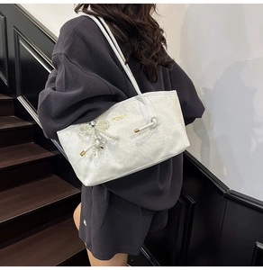 Detail of white faux leather tote bag with snake skin texture and pearl bow charm