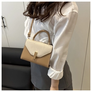 Detail of beige woven flap and khaki leather handbag worn by model in a home setting