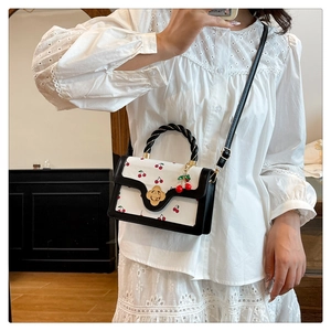 Detailed view of white cherry print handbag featuring twisted handle and gold floral clasp