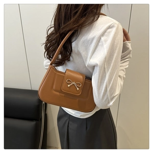Detail of a brown vintage baguette bag featuring a gold metal bow on smooth leather