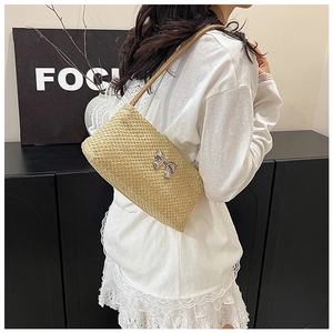 Detail of hand-woven straw shoulder bag with metallic silver bow and slim leather strap