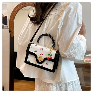 Detail view of cherry print bag with braided handle and petal-shaped rotating gold lock