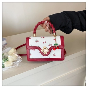 Close-up of woven red handle and cherry print pattern with gold flower metal clasp