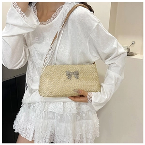 Detail of light straw woven shoulder bag featuring a silver metal bow buckle accent