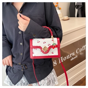 Close-up of cherry print small square bag with red twisted handle and golden flower clasp