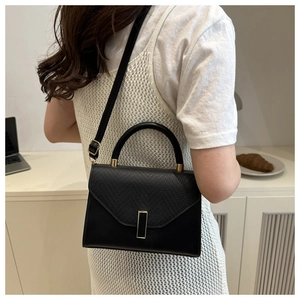 Fashionable black crossbody bag with lizard texture detail shown on a model's shoulder