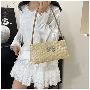 Detail of straw shoulder bag featuring metallic bow and brown strap for summer fashion