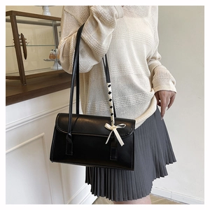 Détail du sac à bandoulière noir avec sangle à damier et nœud en ruban crème