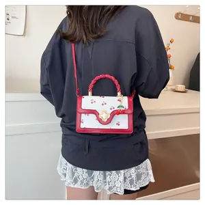 Detail of cherry pattern bag featuring woven red handle and floral gold clasp on a model