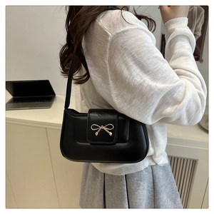Détail d'un sac baguette noir avec nœud doré porté par un mannequin dans un bureau